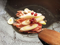 にんにくを炒めているフライパンに、豚肉と長ネギ、鷹の爪を加える。