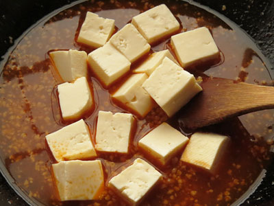 鶏がらスープの素を入れたフライパンに下茹でした豆腐を入れる