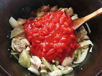 炒めた玉ねぎと鶏もも肉にトマト缶を入れる