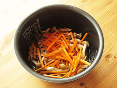 米と調味料の入った炊飯器にニンジンとしめじ、舞茸を入れる