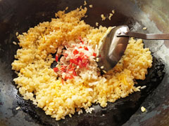 ご飯を炒めている中華鍋に、切り分けたチャーシューの具材を入れる。