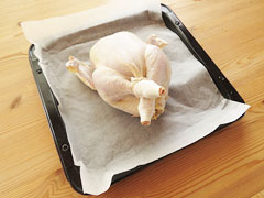 クッキングシートを敷いたオーブンの天板に丸鶏を置く