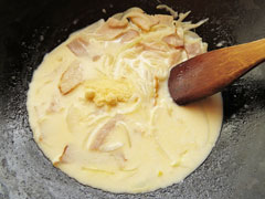 牛乳で材料を煮ているフライパンに、パルメザンチーズと醬油を入れる