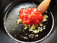 にんにくと玉ねぎを炒めているフライパンに、トマト缶の中身120～150gを入れる。