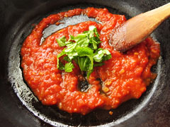 トマトを煮詰めているフライパンに、みじん切りにしたバジルの葉を入れる。