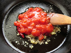 玉ねぎを炒めているフライパンにトマトの水煮缶150gを入れる。