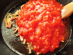 玉ねぎとベーコンを炒めているフライパンにトマト缶を加える。