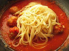 フライパンで煮込んでいるミートボールのトマト煮込みに、茹でたスパゲティを入れる。