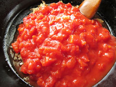 にんにくとベーコン、玉ねぎを炒めているフライパンにトマト缶の中身を入れる。