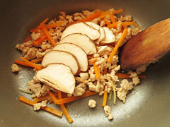 鶏ひき肉と人参を炒めている鍋に、切り分けた椎茸のかさと軸を入れる。