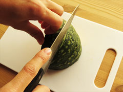 まな板に置いたかぼちゃを、手でしっかりと固定して切り分ける。