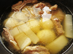 豚バラ軟骨と大根を煮込んでいる鍋に、ゆで卵と調味料を加える。