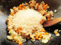 玉ねぎとにんじん、鶏肉を炒めているフライパンに生米を入れる。