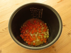 炒めた米の入った炊飯器の内釜に、玉ねぎとにんじん、溶かしたコンソメ、水を入れる。