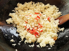 ごはんを炒めている中華鍋にカニカマと長ネギを加える。