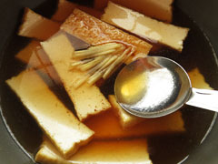 厚揚げを炒めている鍋に生姜とだし汁、酒、醤油、みりん、砂糖を加える。