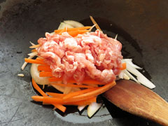 にんにくを炒めているフライパンに豚肉と玉ねぎ、にんじんを入れる。