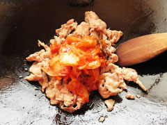 豚肉を炒めているフライパンにキムチを入れる。