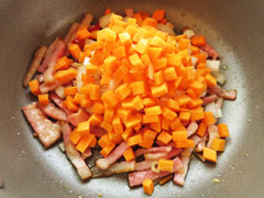 ベーコンとにんにく、鷹の爪を炒めている鍋に、玉ねぎとにんじんを入れる。