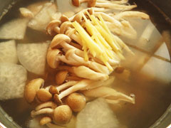 大根とにんじんを煮込んでいる鍋に、鶏むね肉としめじ、千切り生姜、調味料を入れる。