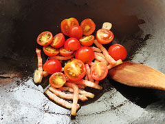 ベーコンとにんにくを炒めているフライパンに、ミニトマトを加える。