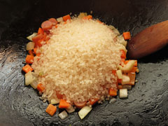 具材を炒めているフライパンに生米を入れる。