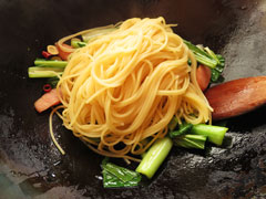 小松菜を炒めているフライパンに、茹で上がったスパゲッティとスパゲッティの茹で汁お玉半分を入れる。