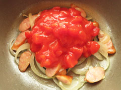 ソーセージと玉ねぎを炒めている鍋に、トマト缶半分をあける。