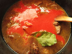 牛肉と野菜を炒めている鍋に、赤ワインとトマトジュースを注ぐ。
