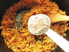 ミートソースの具を炒めている鍋に、小麦粉を加える。