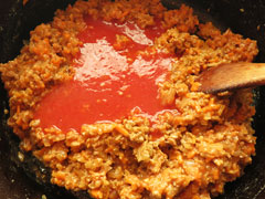 ミートソースの具を炒めている鍋にトマトジュースを加える。