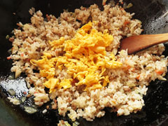 ご飯を炒めているフライパンに、炒り卵と味付け用のたれを入れる。
