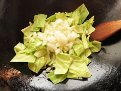 ひき肉と中華蒸し麺を炒めたフライパンに、キャベツと玉ねぎを入れる。