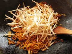 カレー焼きそばを炒めているフライパンに、もやしを入れる。