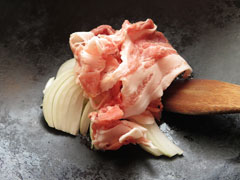 にんにくを炒めているフライパンに、豚肉と玉ねぎ、鷹の爪を入れる。