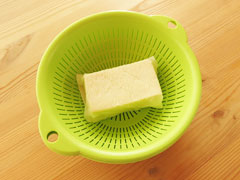 キッチンペーパーに包んでざるに入れた絹豆腐。