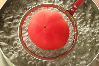 網を使ってトマトを沸騰した湯に入れる。