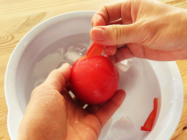 湯にくぐらせたトマトの皮を手で剥く。（トマトの湯むき）