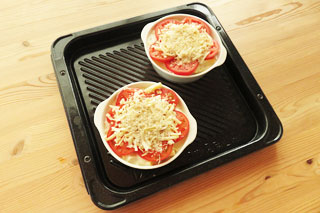 ピザ用チーズを盛り付け、パン粉とパルメザンチーズをちらした、焼く前の焼きトマトのマカロニグラタン。