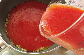 にんにくを炒めている鍋にトマトジュースを注ぐ。