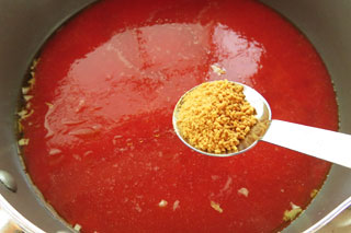 煮込んでいるトマトスープにコンソメをくわえる。