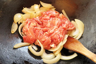 玉ねぎを炒めているフライパンに、豚こま肉をくわえる。