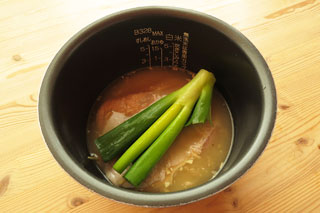 炒めた米と水の入った炊飯器の内釜に、下味をつけた鶏もも肉とネギの青いところを入れる。