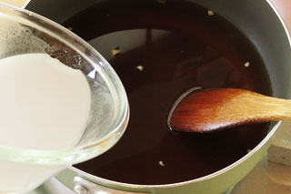 鍋で煮込んでいるインスタントラーメンのスープに、水溶き片栗粉を入れる。