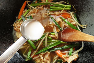 炒めた具材とインスタントラーメンのスープが入ったフライパンに、水溶き片栗粉をくわえる。