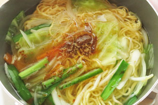 インスタントラーメンの麺と野菜をゆでている鍋に、付属の粉末スープをくわえる。