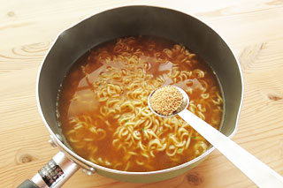 鍋に入ったインスタントラーメンに、計量スプーンで和風だしの素をくわえる。