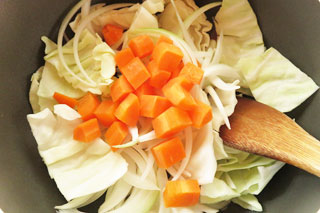 ベーコンとにんにくを炒めている鍋にキャベツと玉ねぎ、にんじんを入れる。