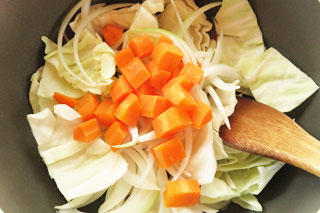 ベーコンとにんにくを炒めている鍋にキャベツと玉ねぎ、にんじんを入れる。