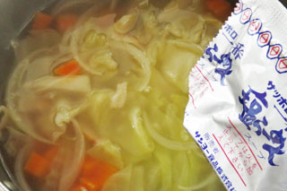 野菜を炒めている鍋に水とインスタントラーメンの粉末スープを入れる。